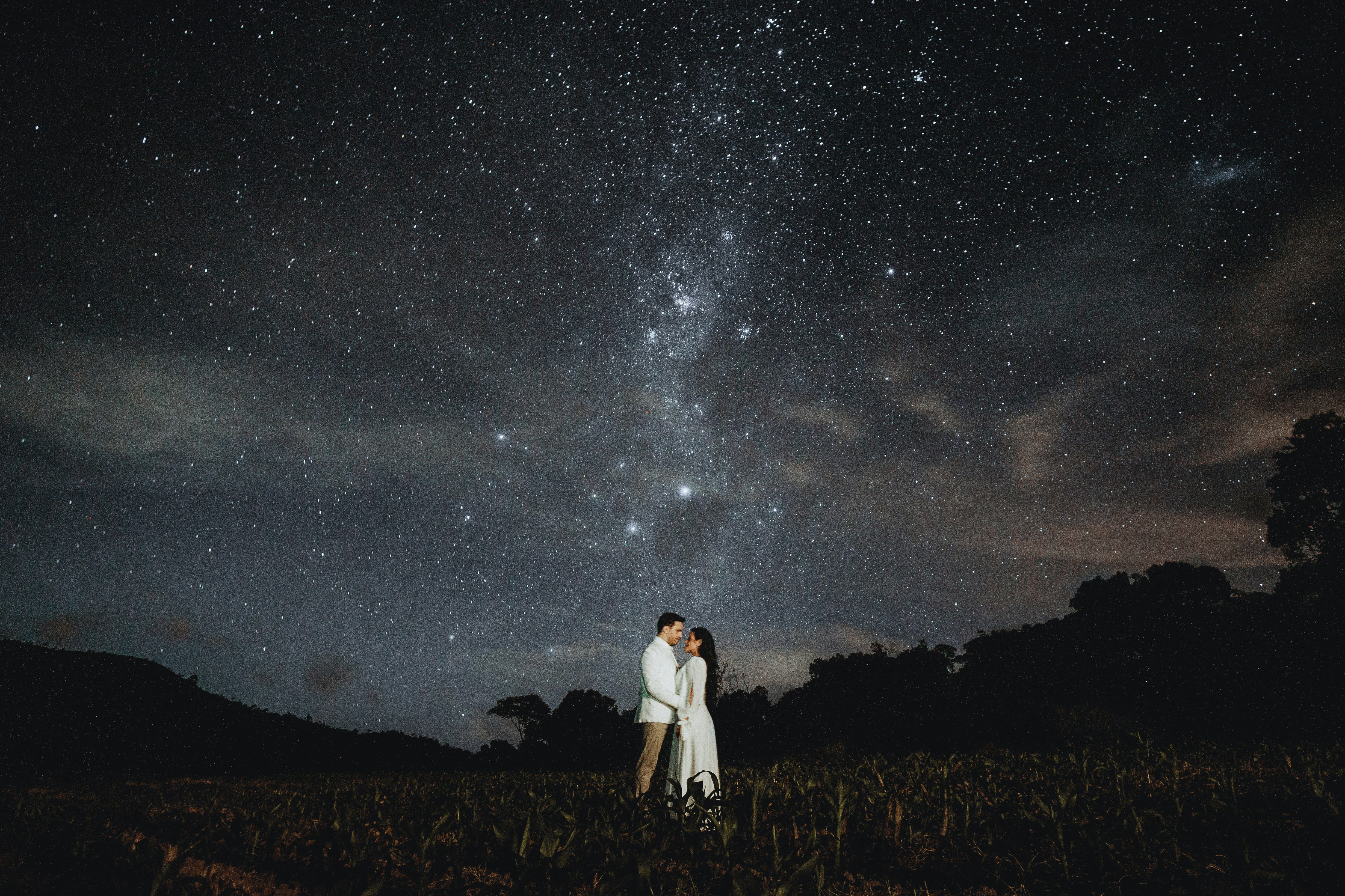 man and woman standing on brown grass field under starry night